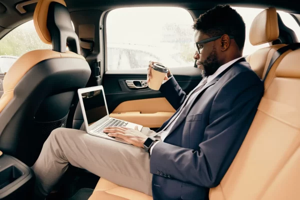 Man drinks coffee and works on the laptop during a car ride.