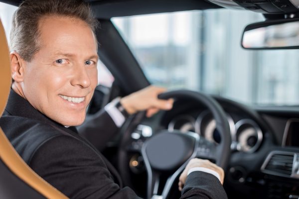 Happy car owner. Rear view of confident senior man in formalwear sitting on drivers place in car and looking over shoulder